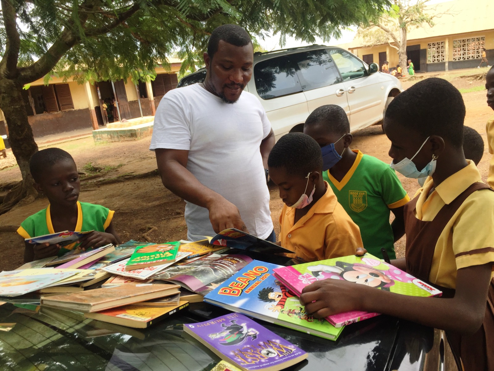 Volunteer distributes books to children from a car trunk