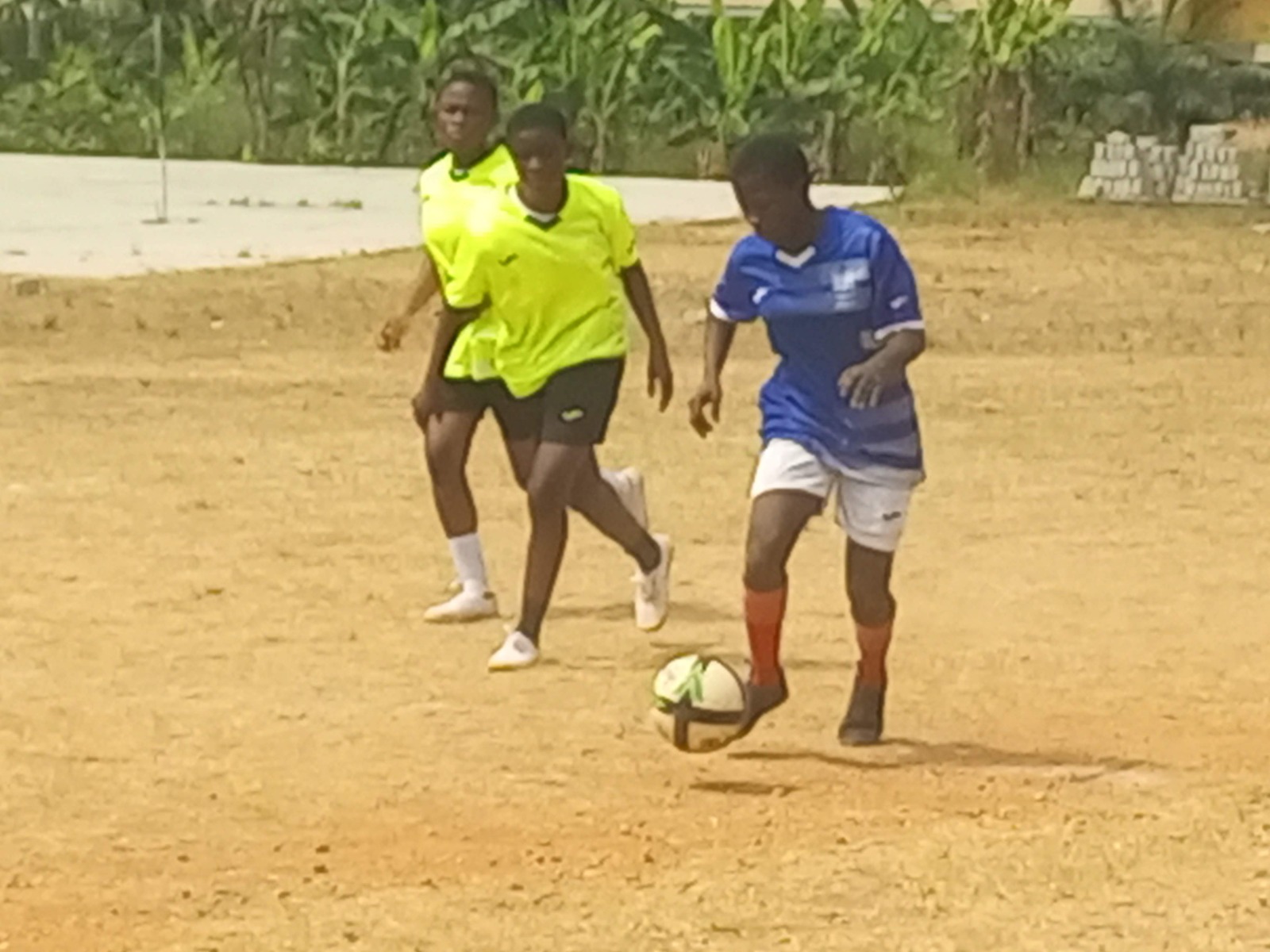 Youth playing football on a community dirt pitch